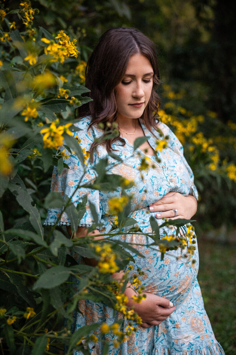 Maternity portrait of a mother looking down at her belly surrounded by yellow flowers. 