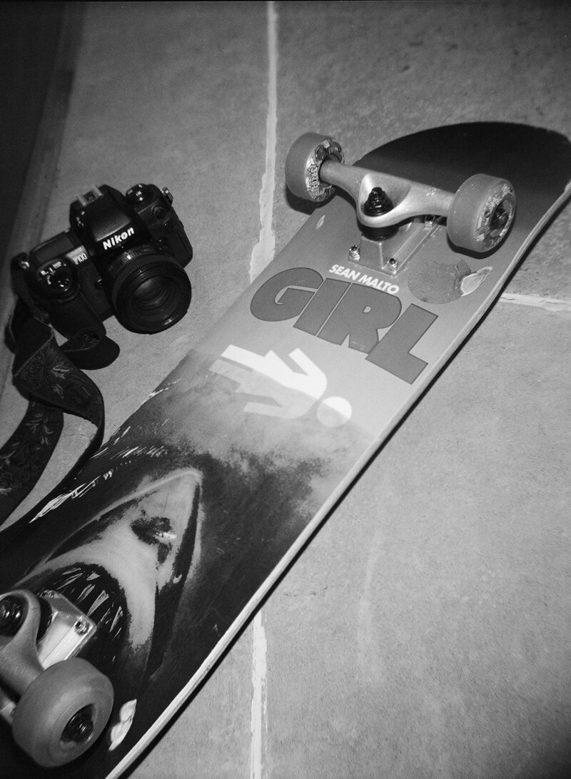 Black and white photo of a skateboard and film camera. Eilish Bailey Photography Documentary Charlottesville Wedding Photographer
