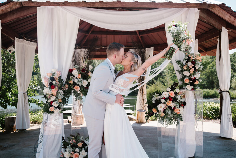 a bride and groom kissing at the end of the cermony and the bride has her bouqet raised in the air