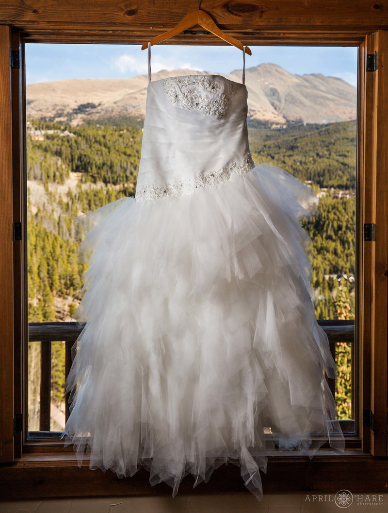 Bride's dress hangs in the window with mountain views off in the distance in her suite at the Lodge at Breckenridge in Colorado