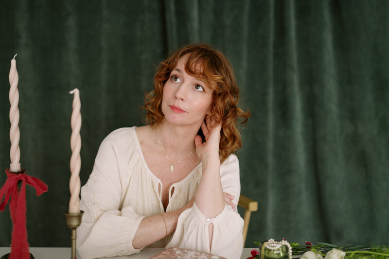 women with red curly hair in front of a green velvet curtain