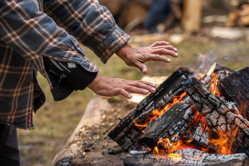 indigenous man warms hands over a fire