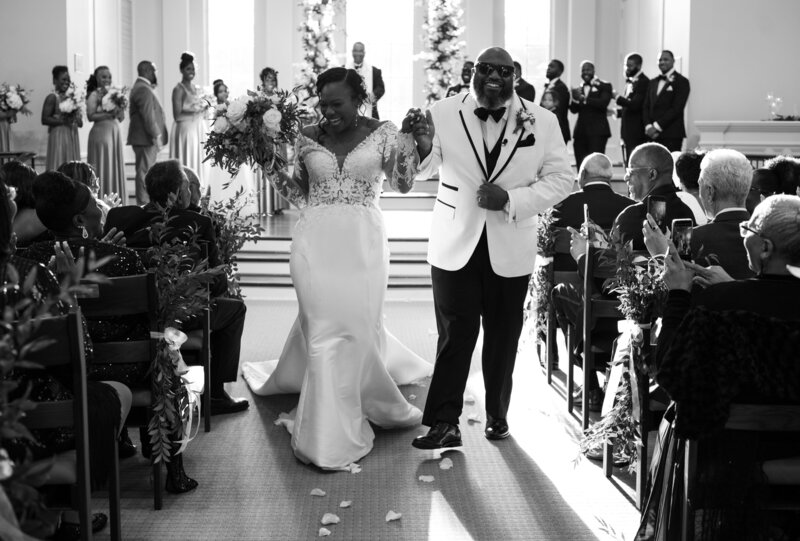 Couple smiling and processing down the aisle while holding hands