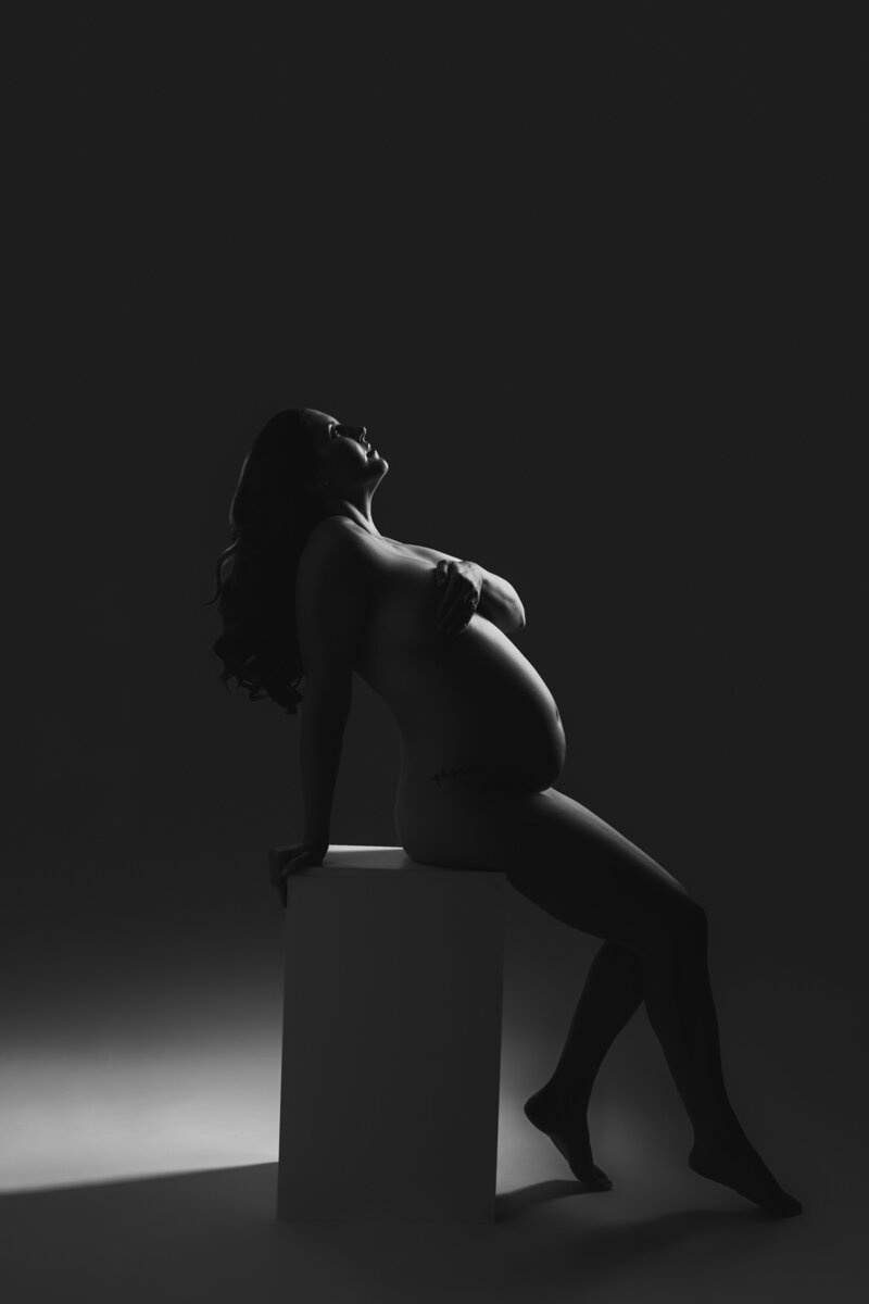 Black and white maternity portrait of nude mother looking off to the side