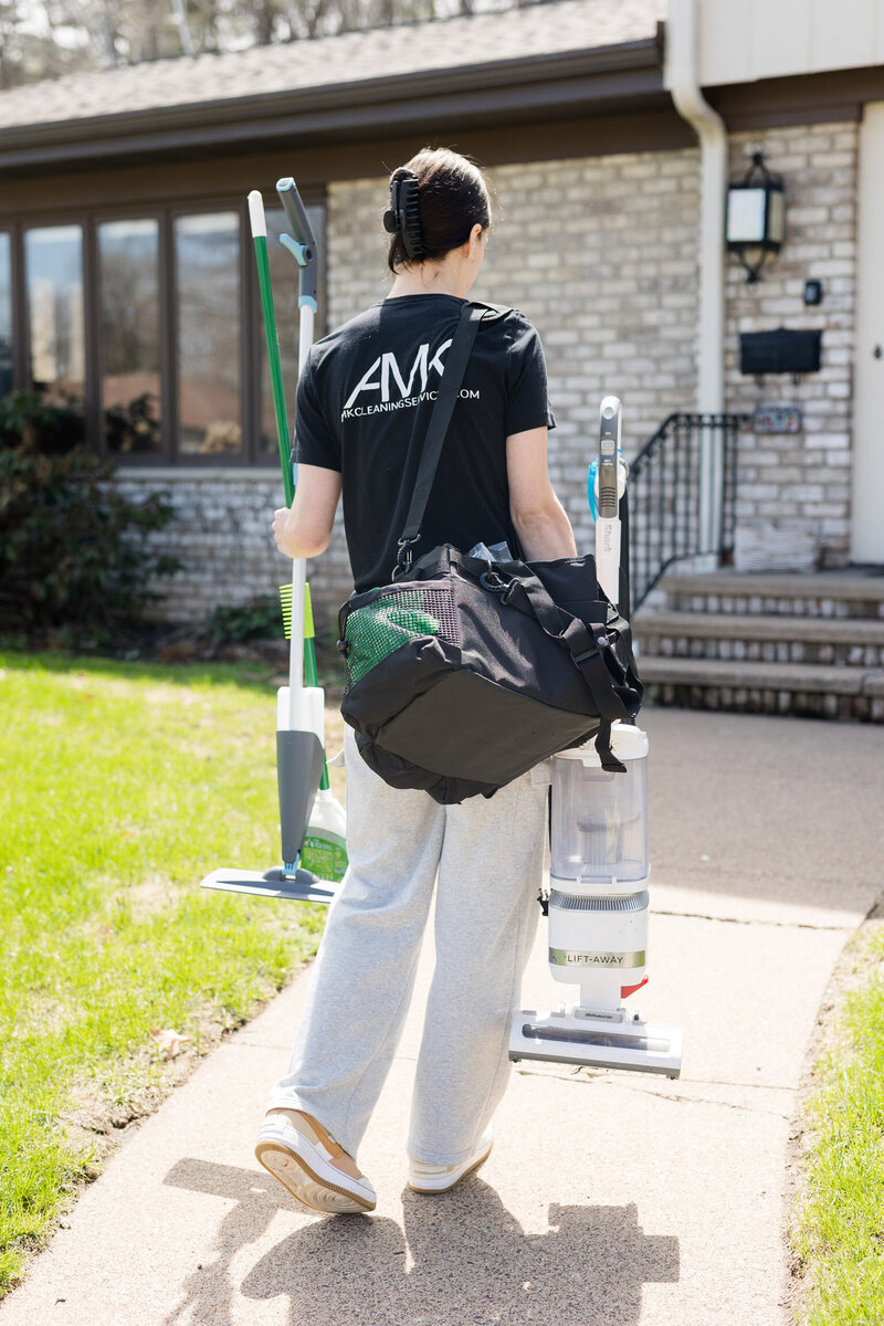 Professional cleaner walking up to a clients home with cleaning supplies