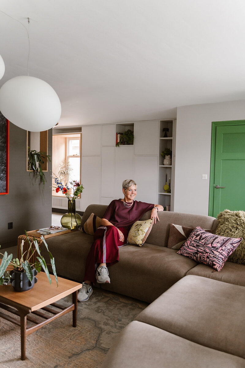 Threa van LOOSZ Interieur & Styling zittend in een comfortabele stoel, met een unieke artistieke muurprint als achtergrond die warmte en karakter toevoegt.