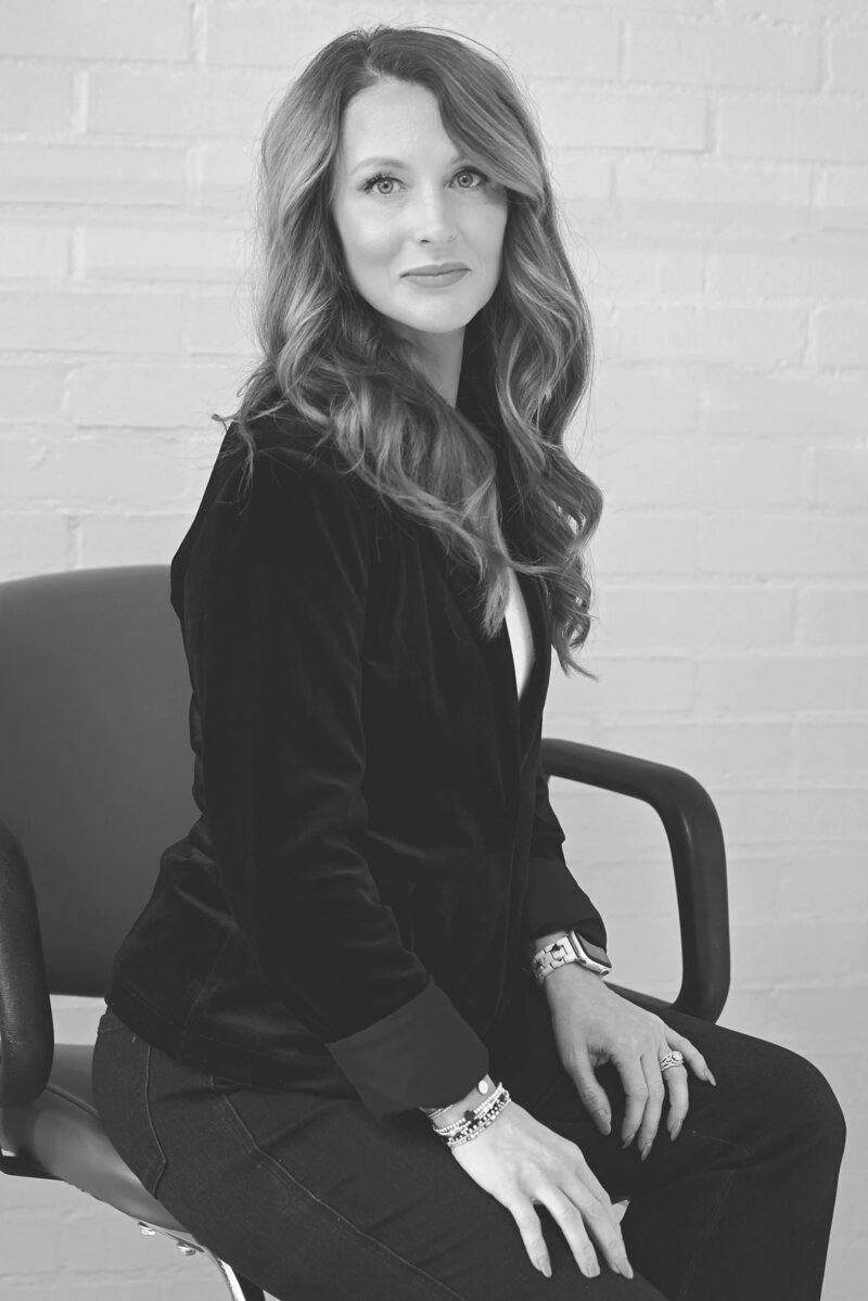 Erica sitting in salon chair, smiling in a black blazer