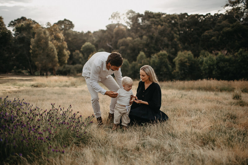 married couple and their baby in a beautiful field at sunset