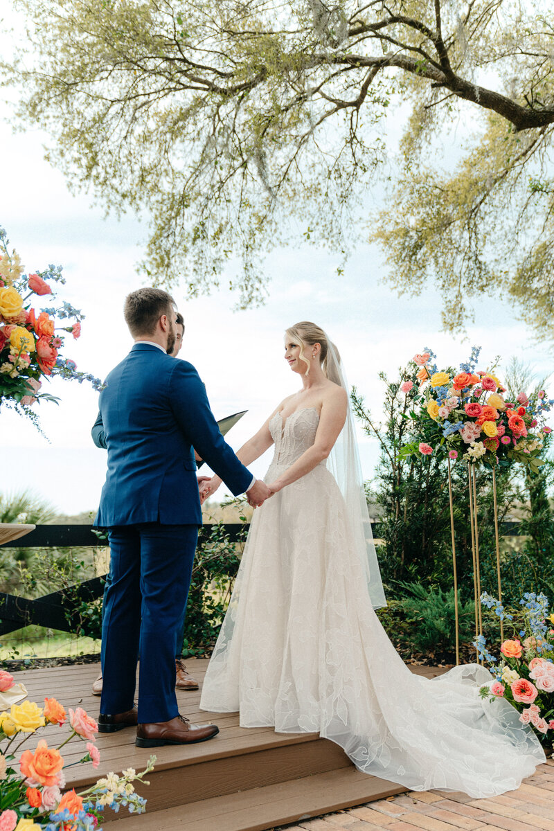 Lake view wedding ceremony at Lakeview Gardens in Lake County, Florida, with the couple exchanging vows beneath tall oak trees.