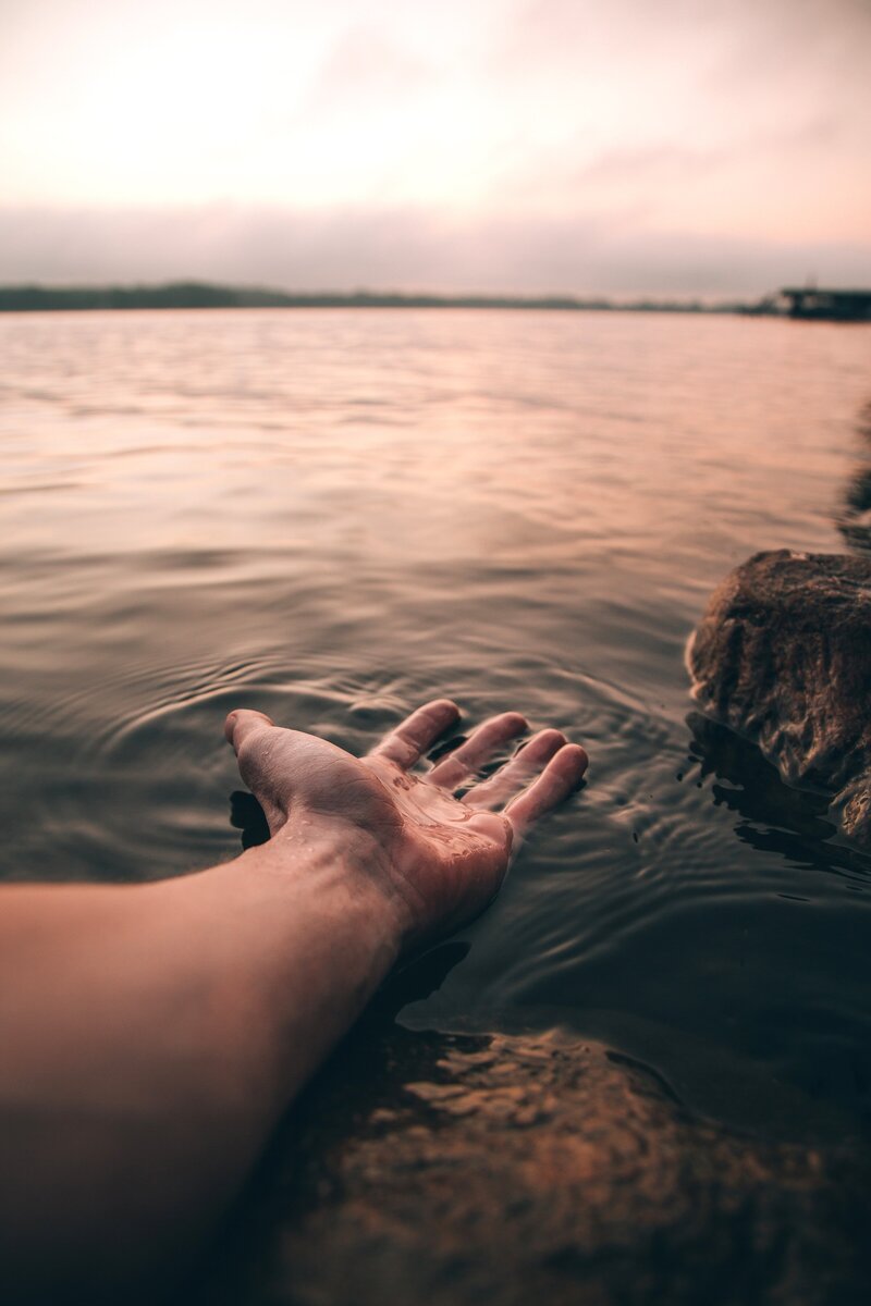 Hand outstretched on top of water on a rocky shore