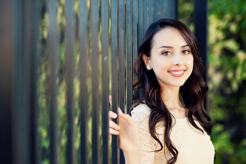 high school senior girl with brown hair leaning up against a black fence in winter park