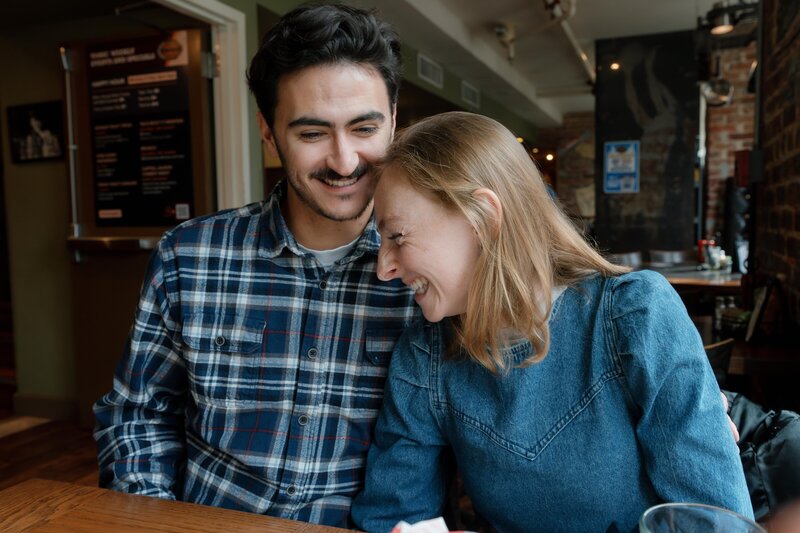 A couple is giggling during their engagement shoot after telling each other a joke at Tonic at Quigley's, a bar in Washington, D.C.