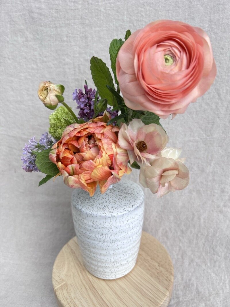 A bud vase arrangement with roses, ranunculus and other fillers representing a Mother's day offering by Wild Child Flower Co.