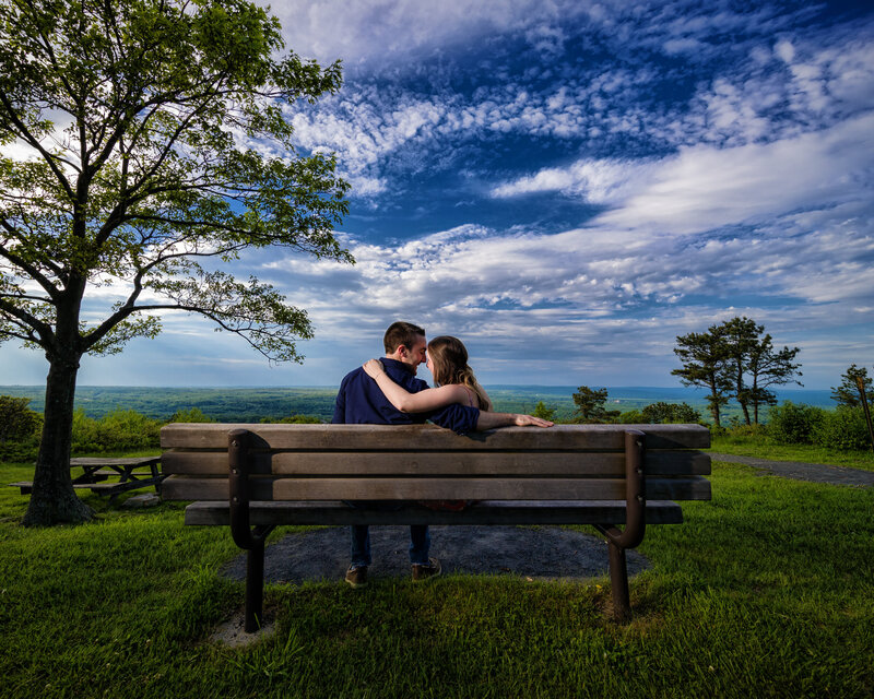 Engaged couple sitting on a rustic bench surrounded by nature in the Poconos during their destination engagement session.