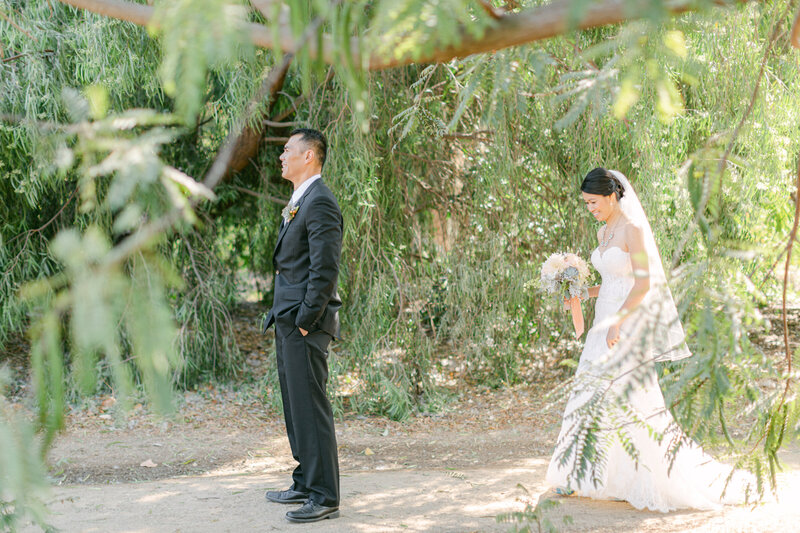 bride walking up to groom with his back towards her for their first look photos