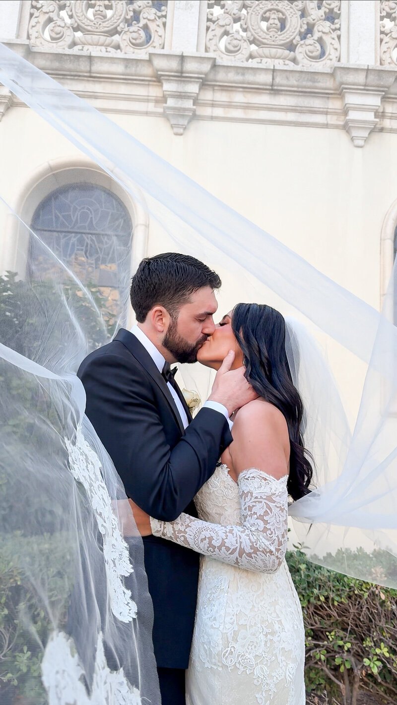 Bride and groom kissing under veil outside of The Immaculata Church in San Diego.