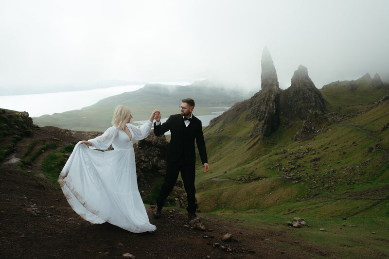 Adventure Elopement Ideas | Eloping couple holds hands and bride tosses her dress as they hike on a Scottish Highland trail