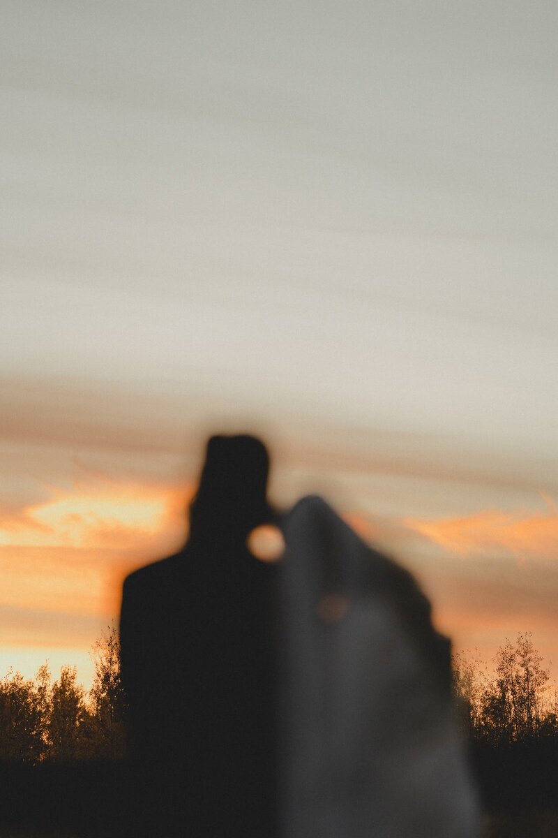 Out of focus wedding couple lean against each other and watch Calgary sunset