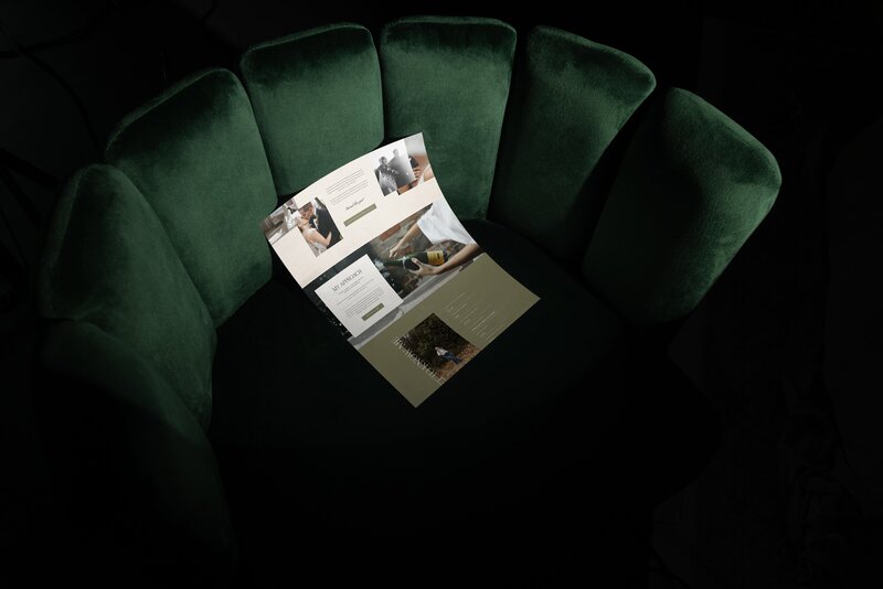 An open brochure with images and text lies on a dark green, scallop-shaped velvet chair under focused lighting, capturing the elegance of brand and web design for small businesses.