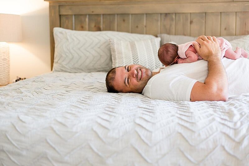 dad laying on the bed with a newborn baby on his chest smiling at Columbia, SC lifestyle newborn photo session