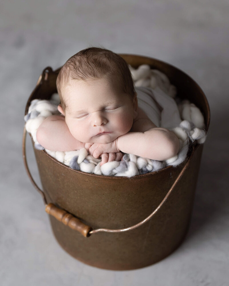 Sleeping newborn in gold bucket with white cloth on gray background