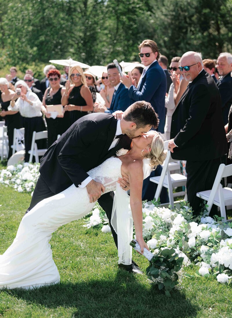 A groom dips and kisses his bride as they walk down the aisle at their wedding ceremony.