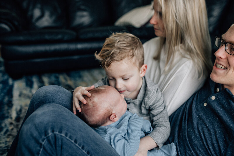 Family and lifestyle photography session with young boy kissing a baby.