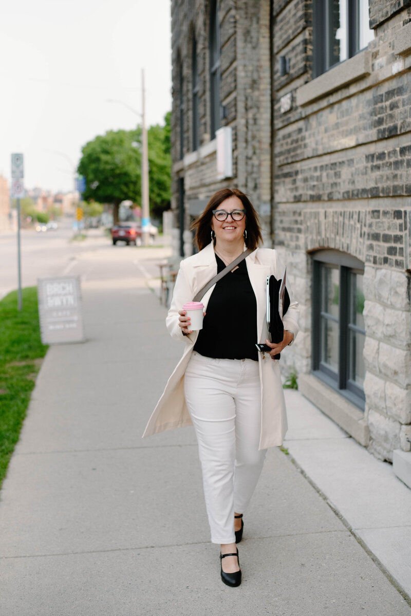 tina grasby stands by home and company office stone wall
