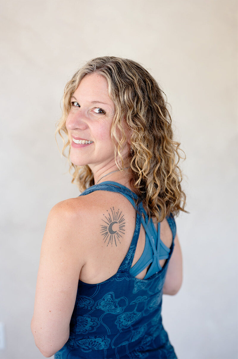 A woman named Heidi with curly hair and a visible tattoo on her back, smiling at the camera.