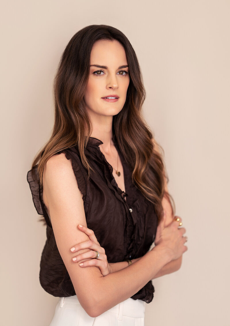 Lee Greene wearing brown blouse against tan/ neutral background
