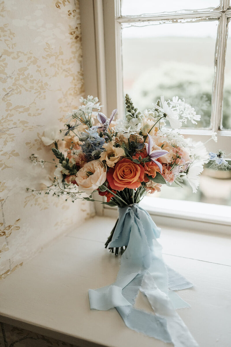 Wedding bouquet of coral and blue flowers at Dewsall Court
