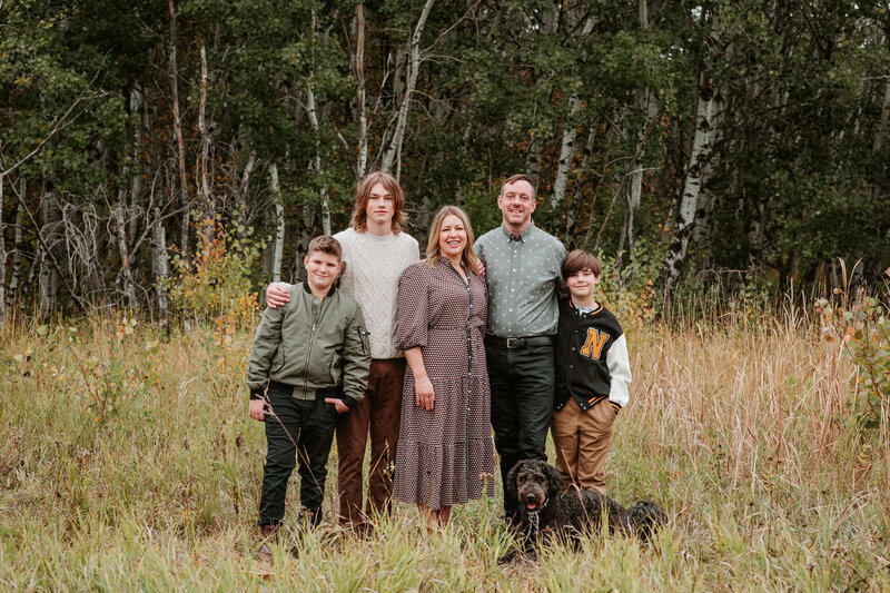 Family standing together against prairie grasses with their dog for new family photos 