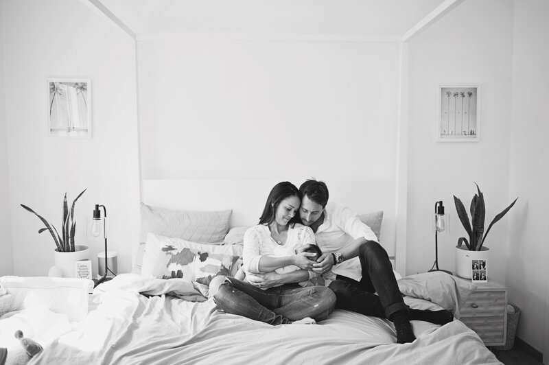 A couple sitting on their bed with their 4 month old son during a photo shoot at their home in Notting Hill, Kensington