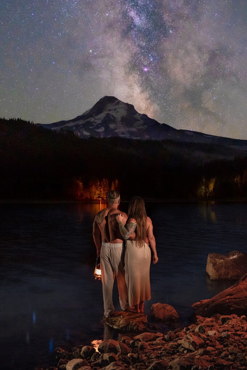 A couple stands in a lake at mt hood under the milky way at night