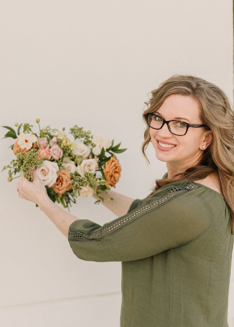 Professional headshot of Kendra, founder of Kendra’s Events, smiling and holding a beautiful bridal bouquet while dressed in business attire. 