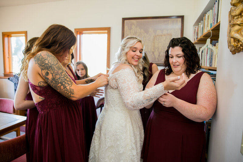 Bride and bridesmaids helping bride put dress on | Rangeley, Maine Wedding Photography