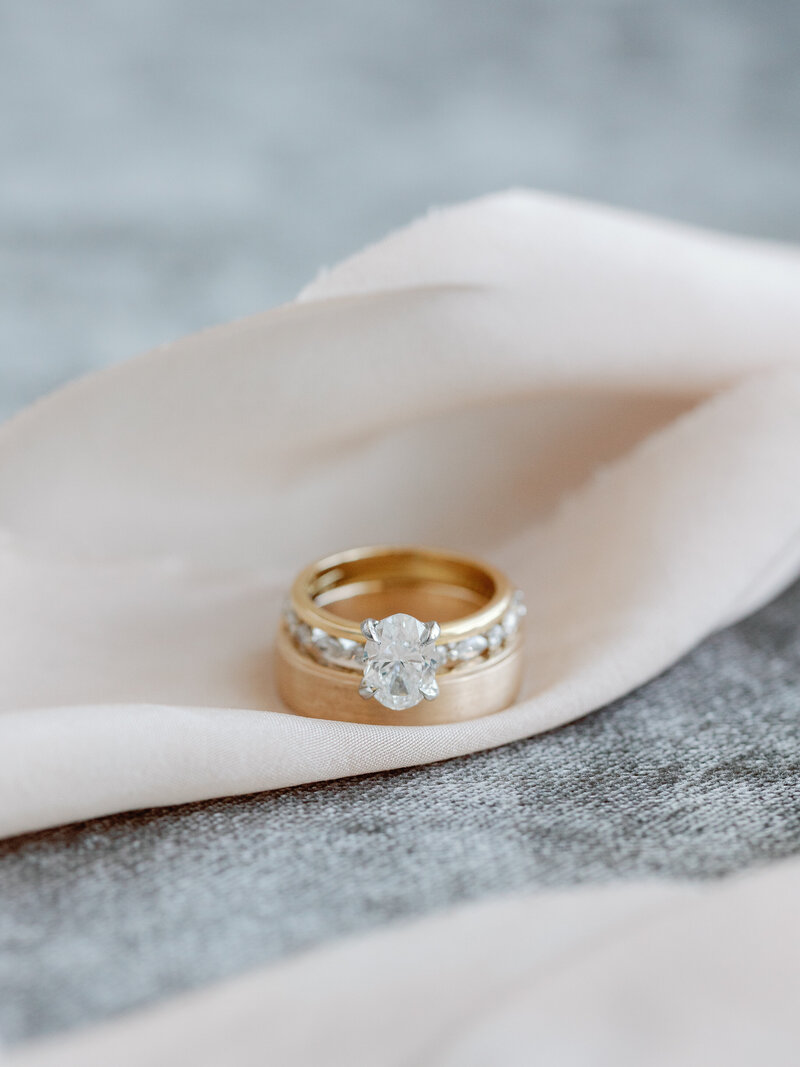 A closeup of the wedding rings with a focus on the oval shaped engagement ring place on top of a blush pink ribbon
