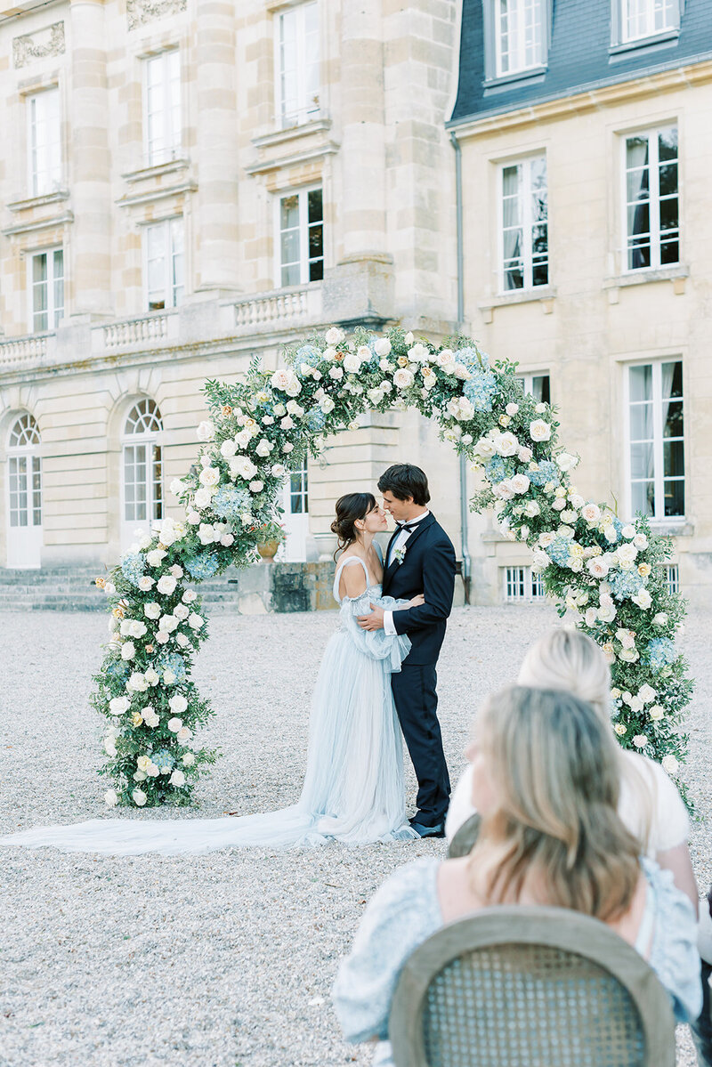 Bröllopsfotograf i Stockholm helloalora Anna Lundgren destination slottsbröllop på Chateau de Courtomer i Normandie Frankrike brudpar vid blosmterbåge med blå hortensior vita och aprikosa rosor