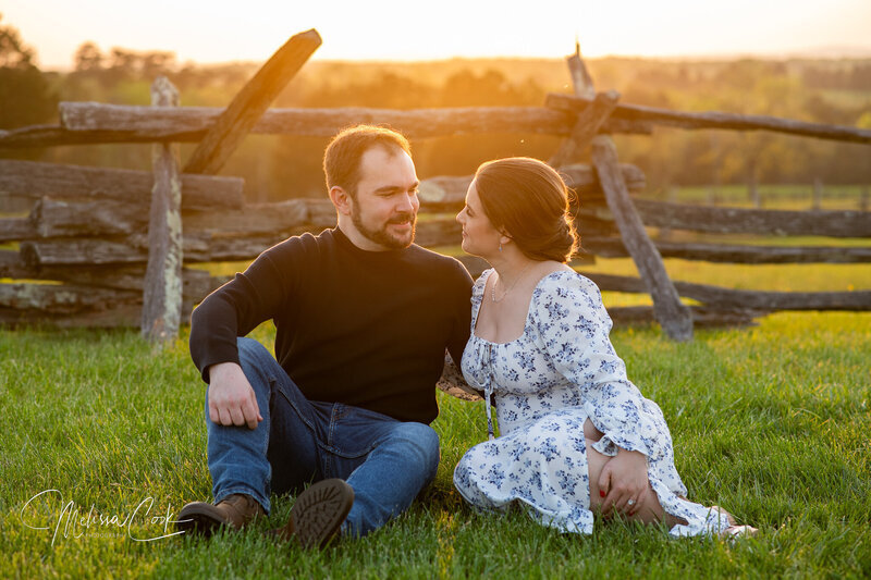 A couple poses for engagement pictures in front of a wooden fence in a field in Leesburg VA