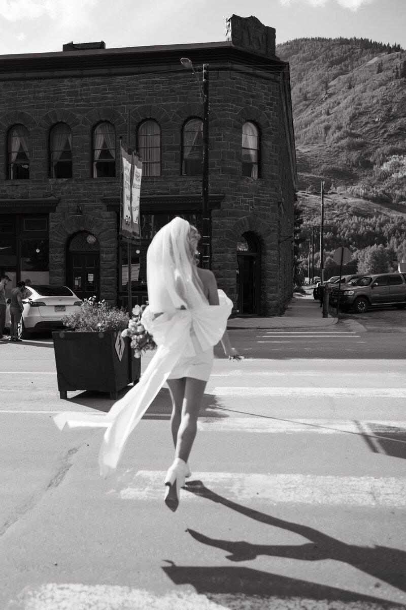 Bride is wearing a short modern wedding dress and running across the street in Silverton, Colorado
