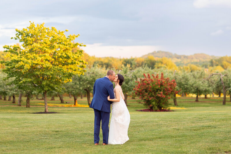 Bride and groom kiss as they walk through an orchard at Connemara House Farm in Topsfield, MA.