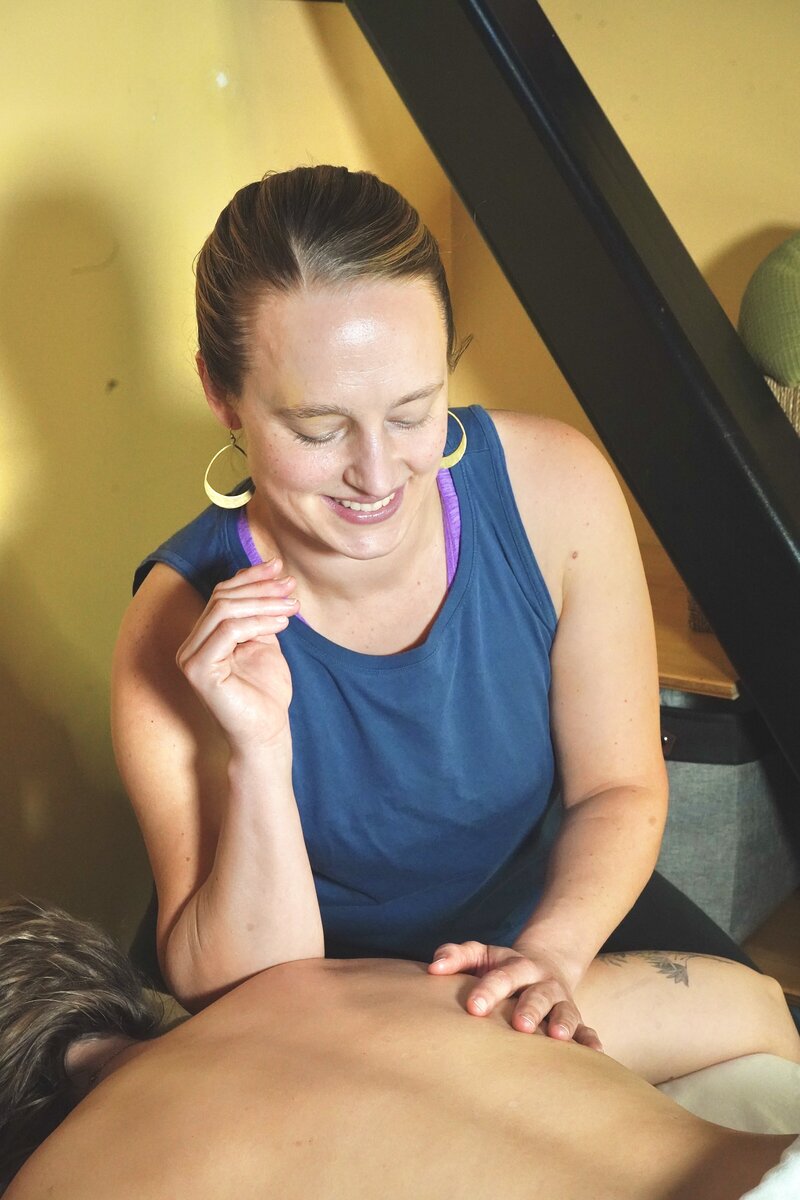 smiling woman using elbow to provide massage to upper back of client