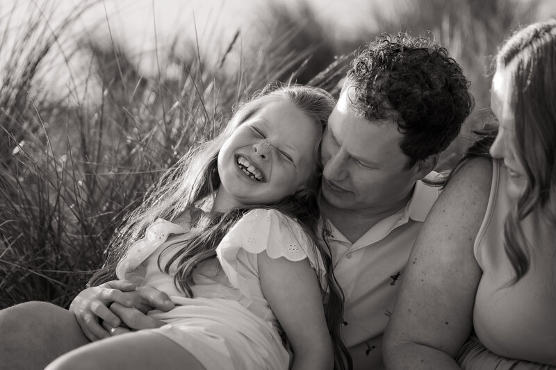 Two boys smiling in a blanket swing being held by their parents on Sussex beach during fun-filled family photoshoot