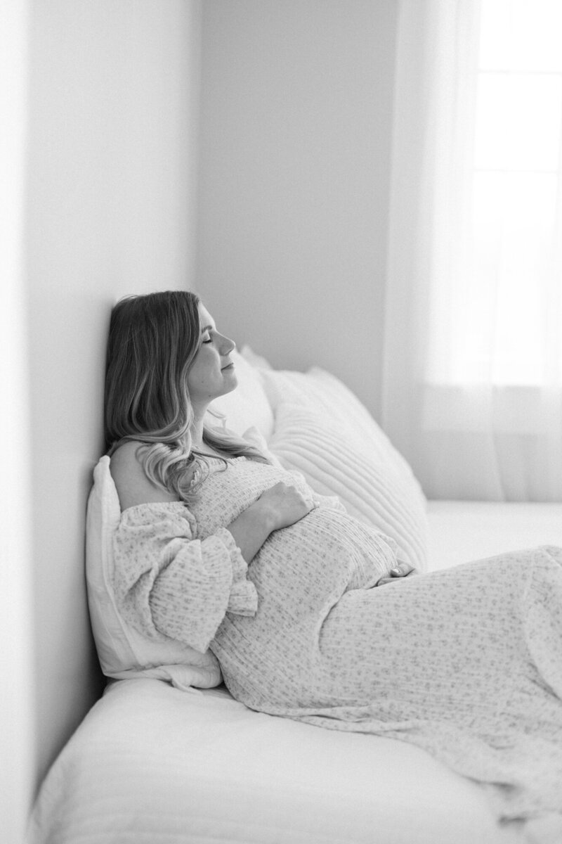Black and white portrait of a mom laying on a bed in a louisville maternity photography studio