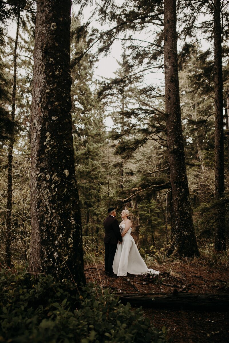 couple stands in midst of brush and tumbleweed smiling and embracing