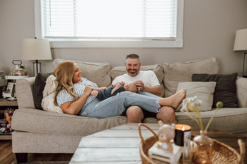 Parents cuddling and casually hanging out on the couch in their living room while holding and talking to their newborn son in St. Louis Missouri. 