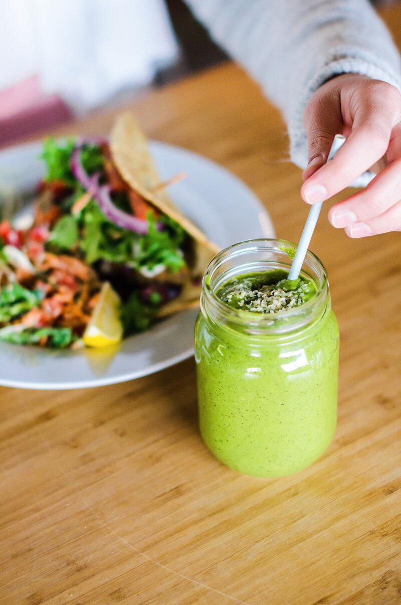 Photo of a green smoothie in a mason jar with a salad in the background