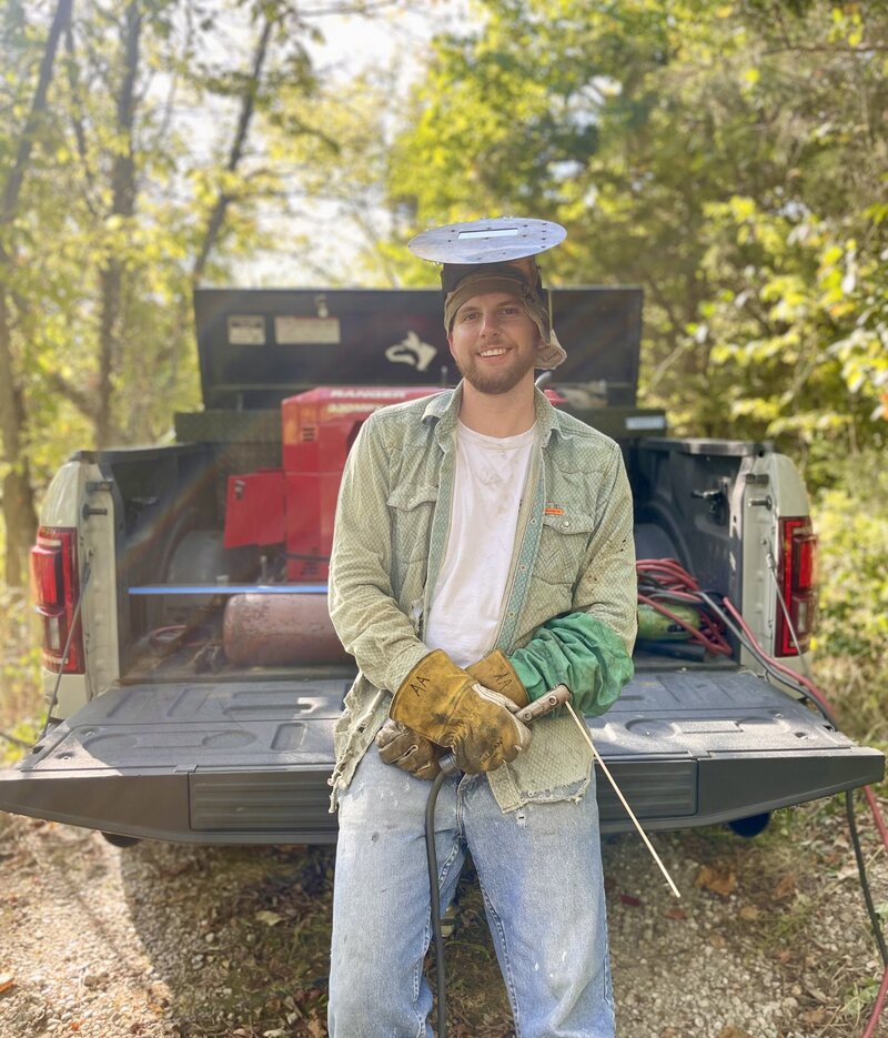 Skilled artisan behind every weld, standing proudly with his trusty welder and rugged truck. Discover the craftsmanship and dedication that fuels every project in our welding workshop.