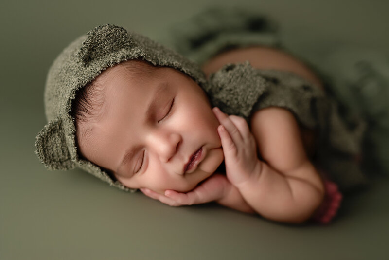 Gentle timber pose with a forest-toned bear bonnet – newborn boy in serene slumber.
