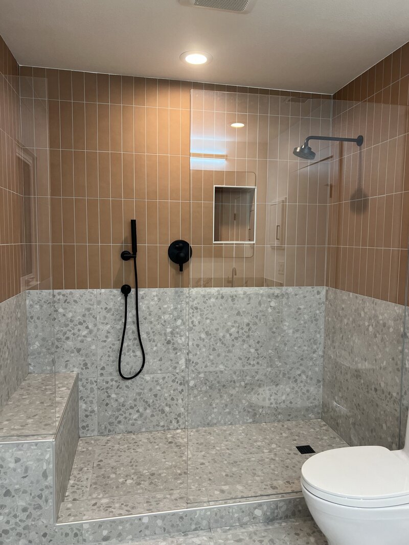 Terra Cotta Subway tiles line the top of a shower with a grey terrazzo print tile on the bottom half and black hardware.